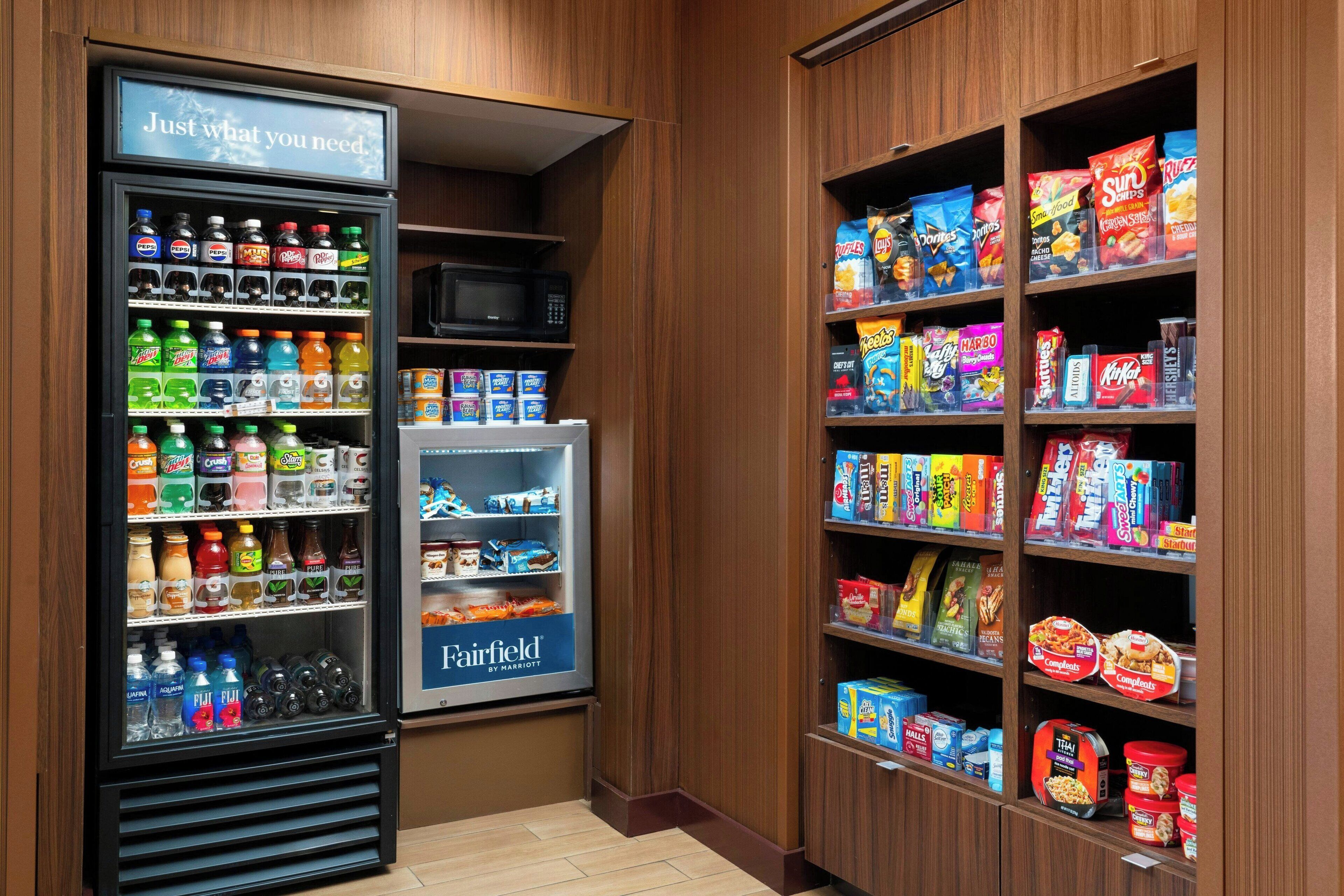 A hotel pantry with a refrigerator stocked with beverages and a microwave.