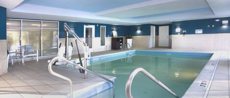 An indoor swimming pool with clear water, a diving board, and a no diving sign.