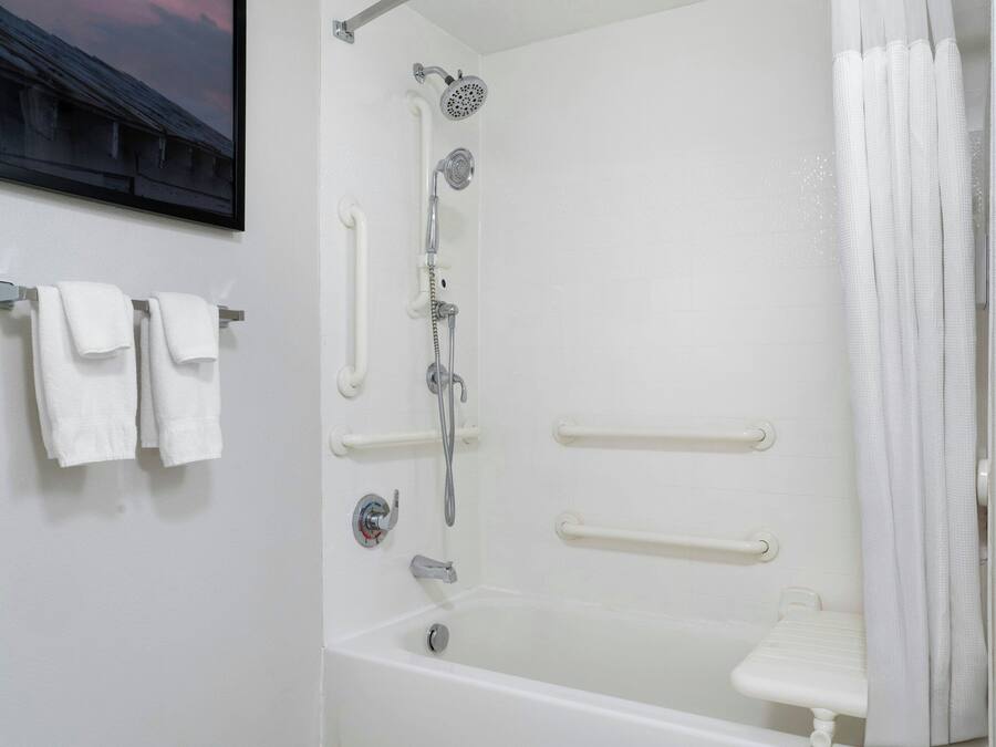 A white bathroom with a bathtub, a shower, and a toilet. There are grab bars installed for safety.