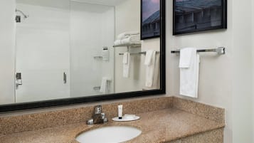 A bathroom with a granite countertop, a sink, a large mirror, and a towel rack with several white towels.