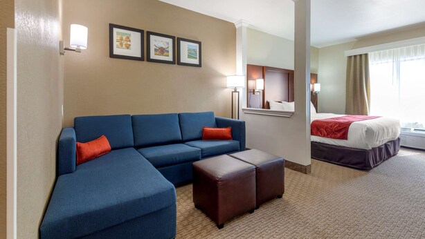 A hotel room with a blue sofa, a bed with a red blanket, and a small table. There are three framed pictures on the wall and a lamp on the nightstand. - Comfort Suites Copperas Cove (Copperas Cove)