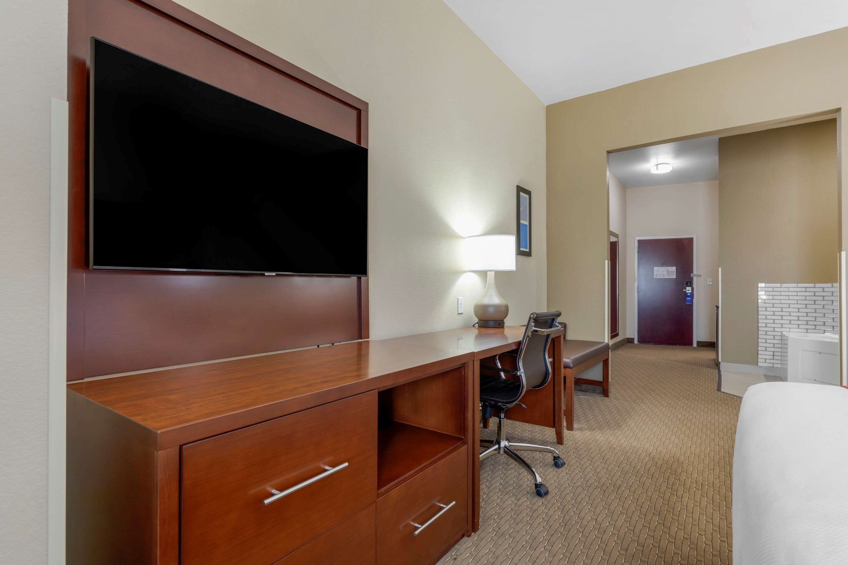 Camera d'albergo con scrivania in legno, televisore a schermo piatto, lampada, sedia e letto.