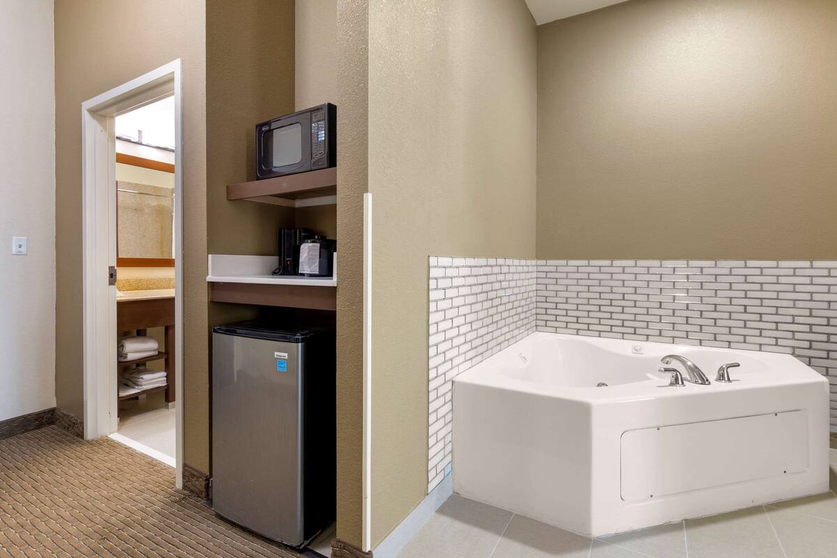 Ein Badezimmer mit einer weißen Badewanne, einem Kühlschrank, einer Mikrowelle und einem Handtuchhalter.