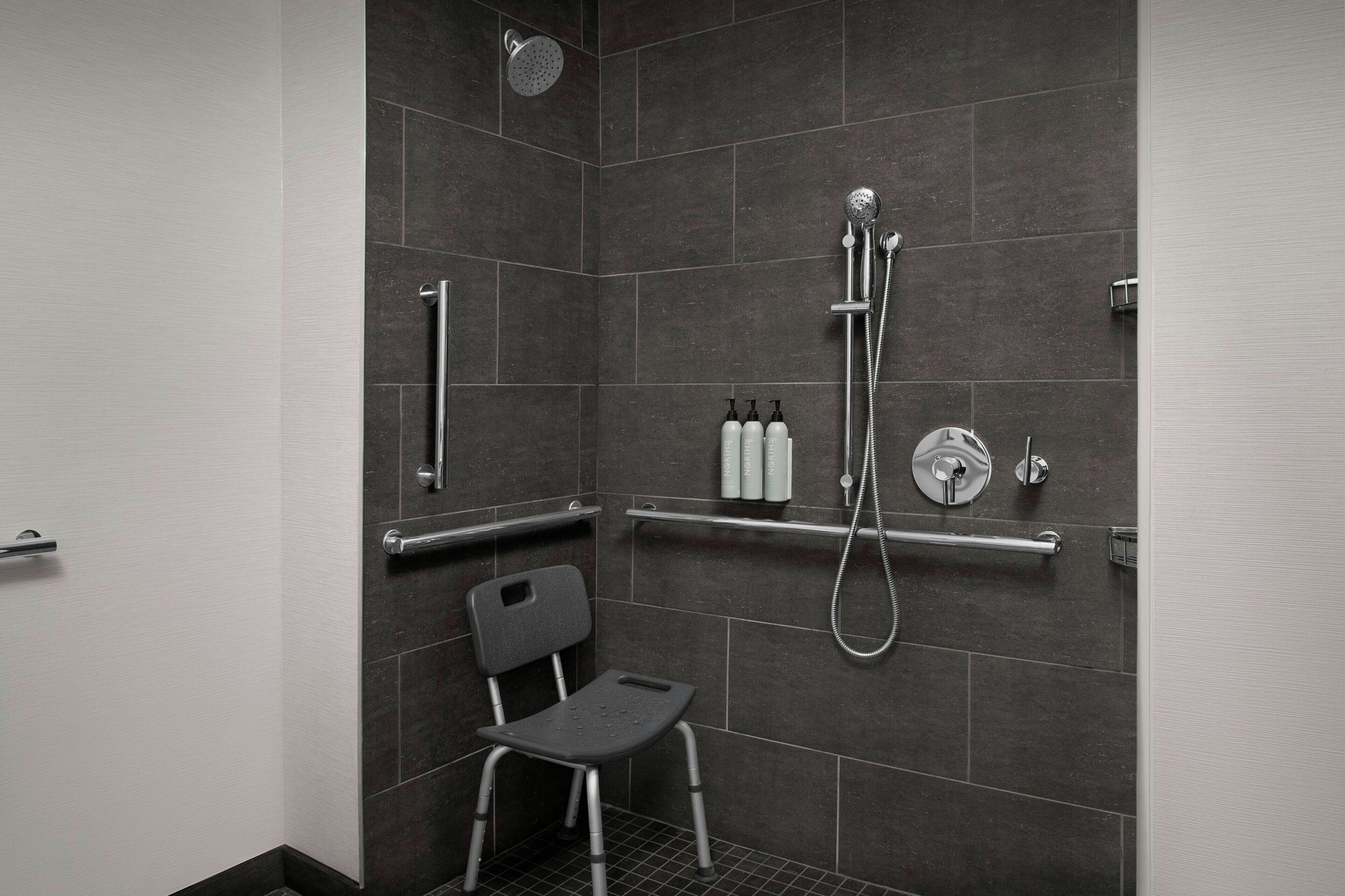 Un área de ducha moderna con ducha de mano y barra de apoyo.