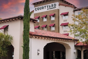Um hotel Courtyard by Marriott com telhado de telhas vermelhas, várias janelas com toldos vermelhos e uma placa visível sobre a entrada.