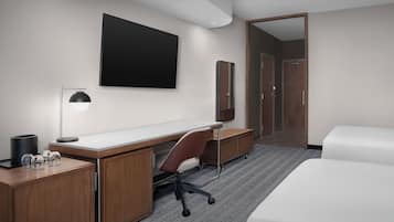 A hotel room with a desk, chair, bed, and a large mirror.