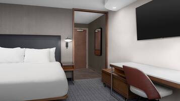 Een moderne hotelkamer met een groot bed, een bureau met stoel, een flatscreen televisie en een spiegel.