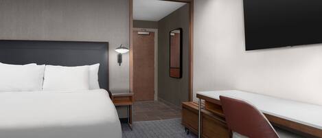 Una habitación de hotel moderna con una cama grande, un escritorio con silla, un televisor de pantalla plana y un espejo.