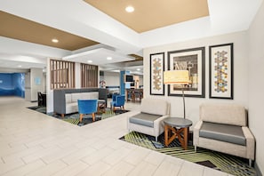 A modern hotel lobby with a seating area, a reception desk, and a dining area.