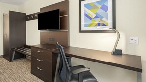 Quarto de hotel com uma escrivaninha, televisão de tela plana, um quadro abstrato emoldurado e uma cadeira.