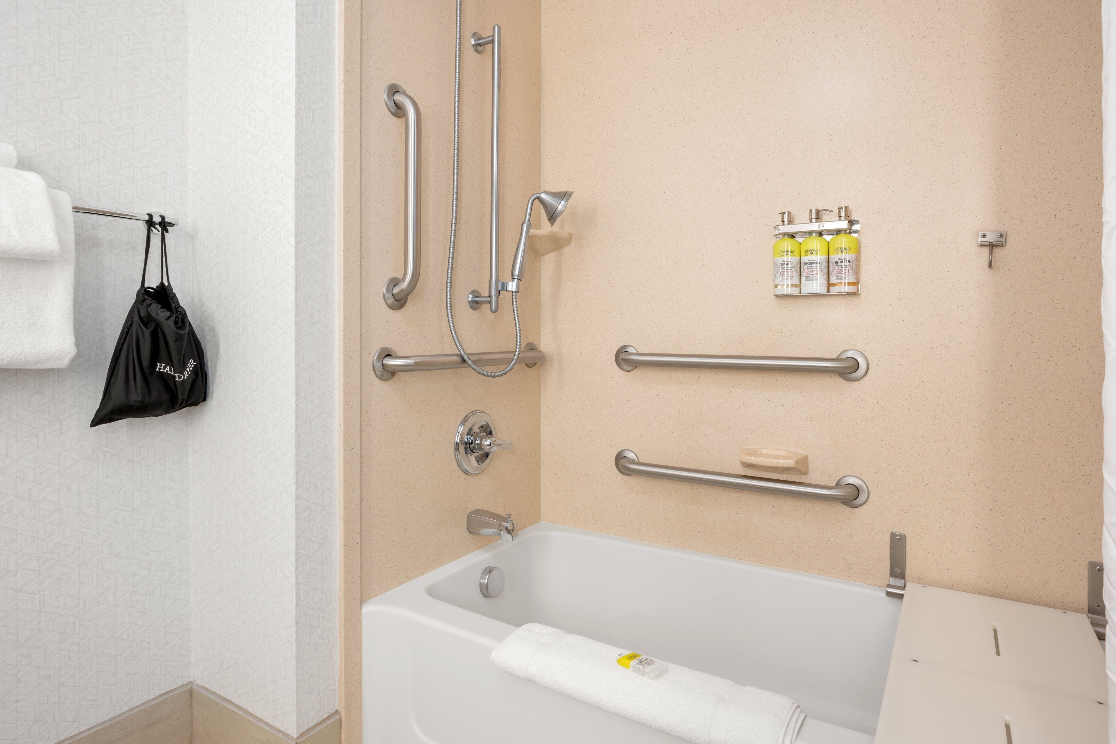 Une salle de bain équipée d’une baignoire, de barres d’appui, d’un porte-serviettes et d’un distributeur de savon.