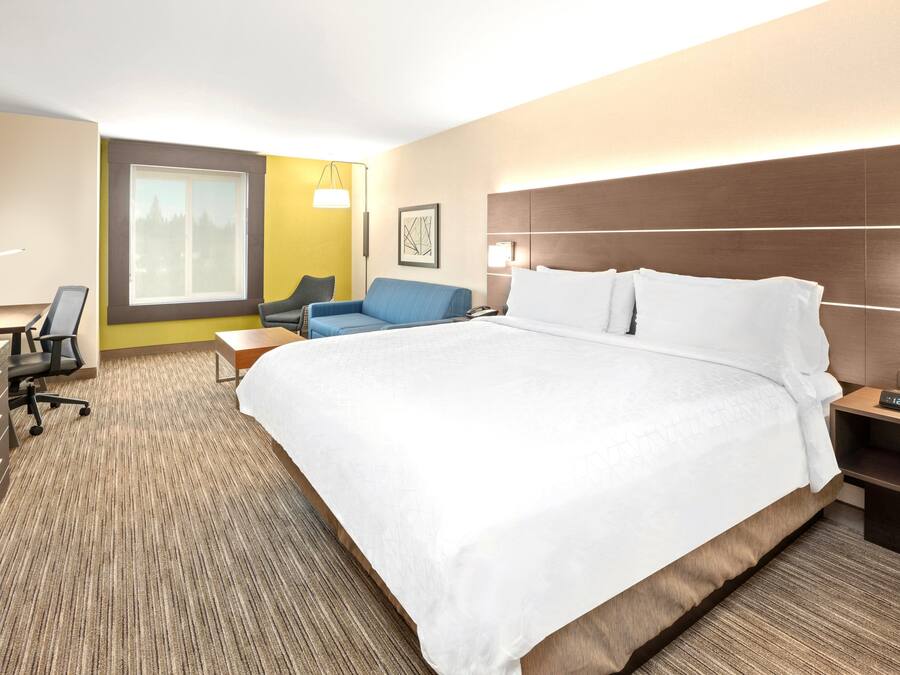 A hotel room with a large bed, a desk with a chair, a sofa, and a nightstand with a lamp.