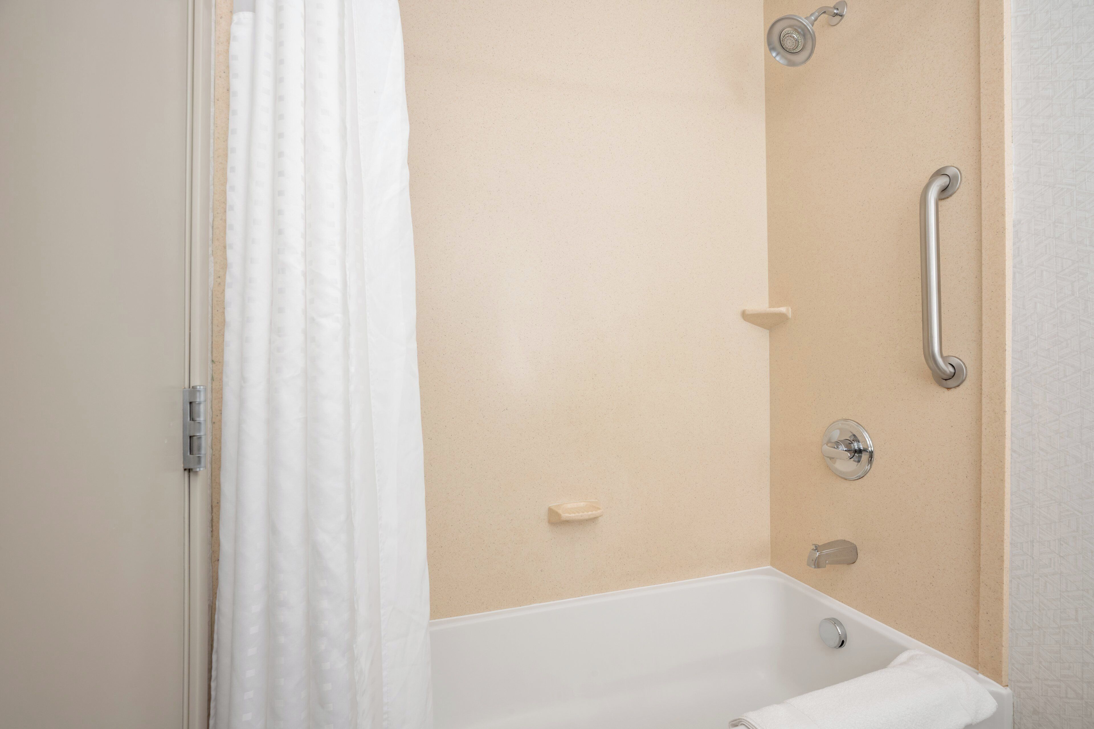 A bathroom with a bathtub, a shower, and a handrail.