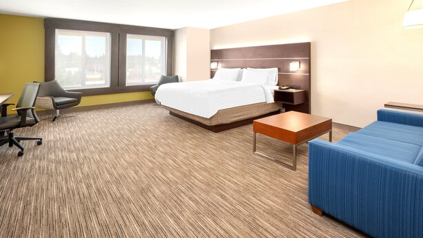 Quarto de hotel com cama, escrivaninha, cadeira, sofá e janela.