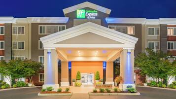 A Holiday Inn Express & Suites building with a covered entrance, potted plants, and a bench.