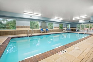 An indoor swimming pool with clear blue water, surrounded by tiled walls and windows.