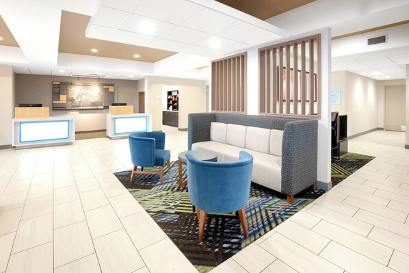 A hotel lobby with a reception desk, seating area, and a kitchenette in the background.