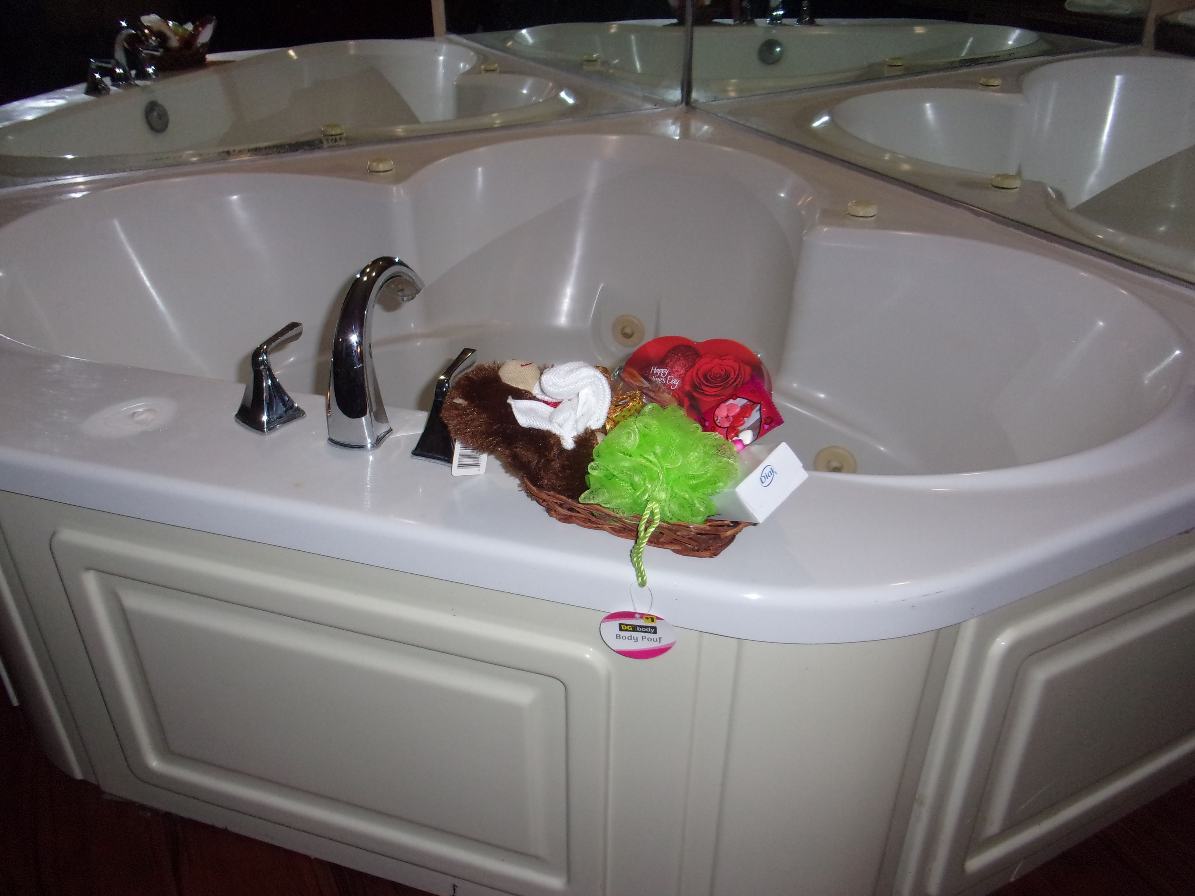 A large bathroom sink with a mirror above it, a bottle of shampoo, and a small gift basket.