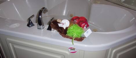 A large bathroom sink with a mirror above it, a bottle of shampoo, and a small gift basket.