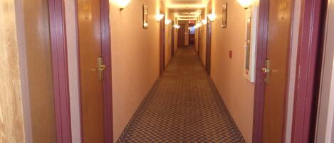 Un passadís d'hotel amb portes de fusta, indicadors de números de habitació i una catifa estampada.