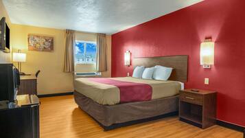 Habitación de hotel con cama, mesita de noche, lámpara y ventana con cortinas.