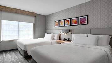 Habitación de hotel con dos camas, un ventanal grande y una pared con cuatro cuadros enmarcados.