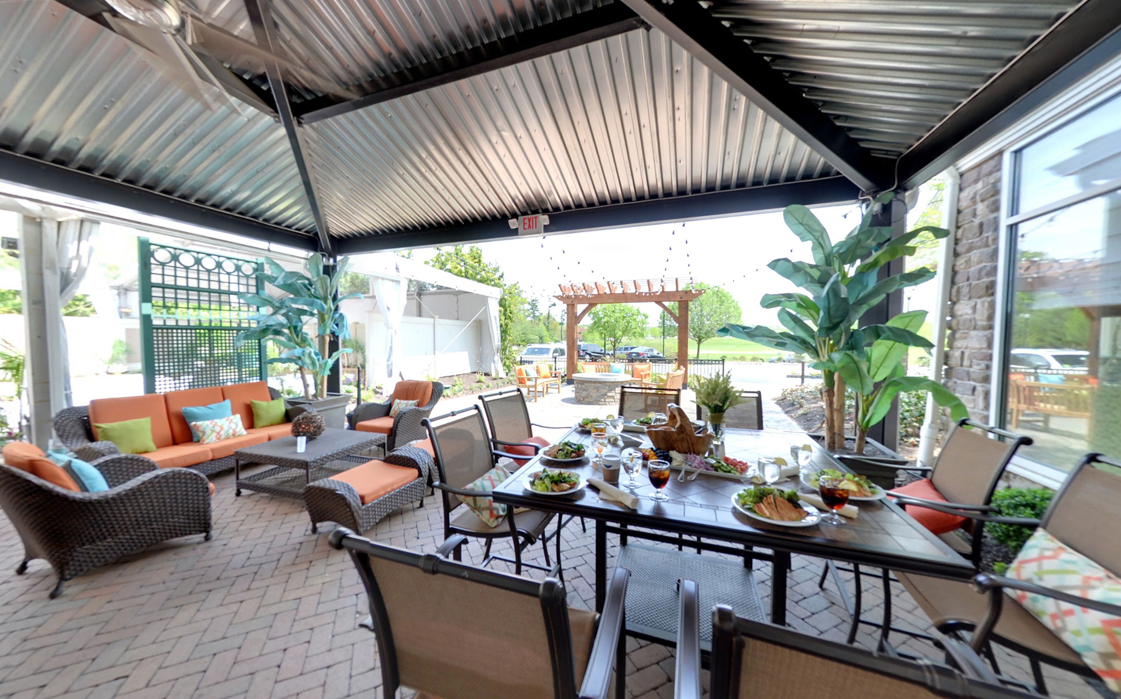 An outdoor patio with a covered dining area, wicker furniture, and a view of the street.