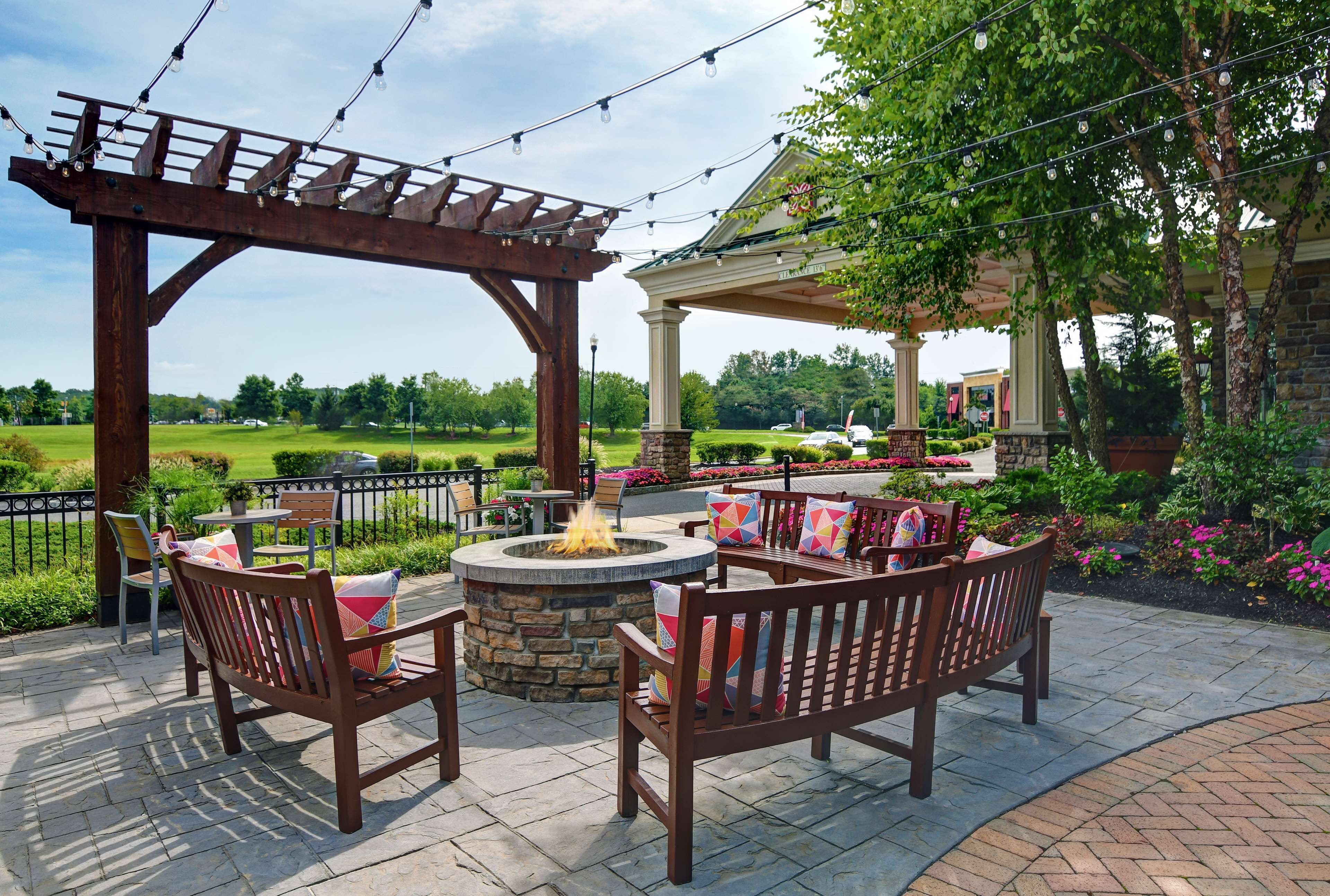 An outdoor patio with wooden furniture, a stone fire pit, and string lights.