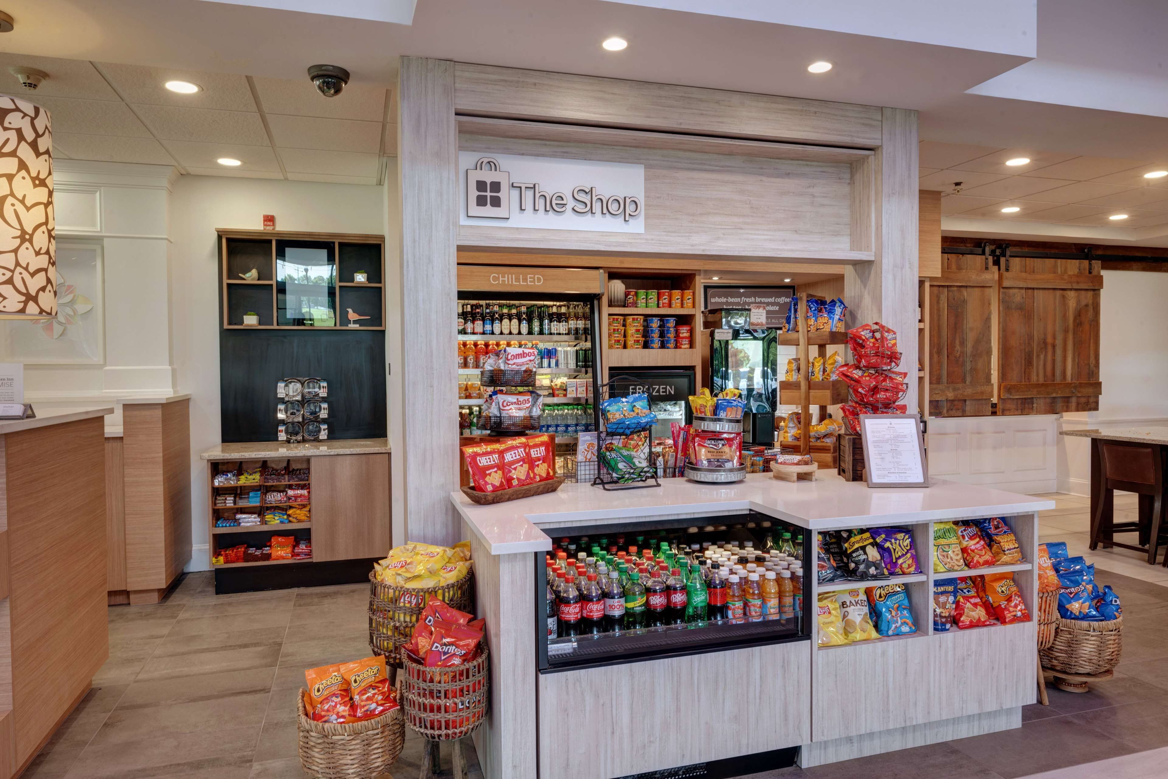 Una tienda con un letrero que dice "The Shop", que ofrece bebidas frías, aperitivos y una variedad de productos envasados.