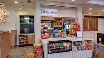 Una tienda con un letrero que dice "The Shop", que ofrece bebidas frías, aperitivos y una variedad de productos envasados.