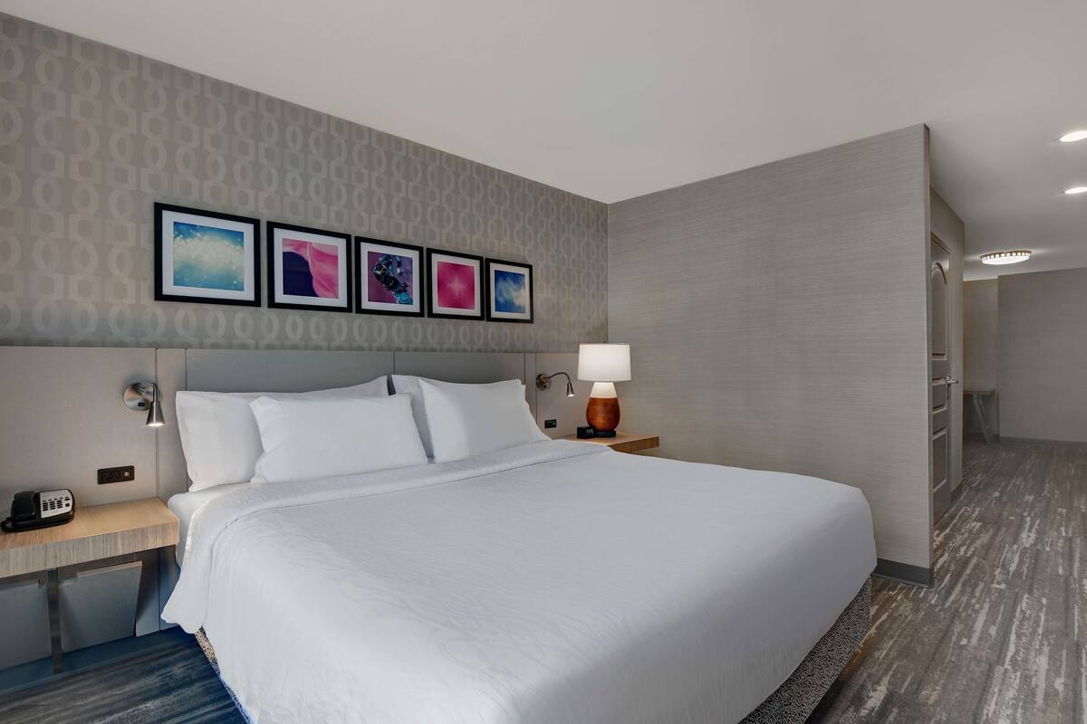 A hotel room with a large bed, a desk with a lamp, and a nightstand with a phone.