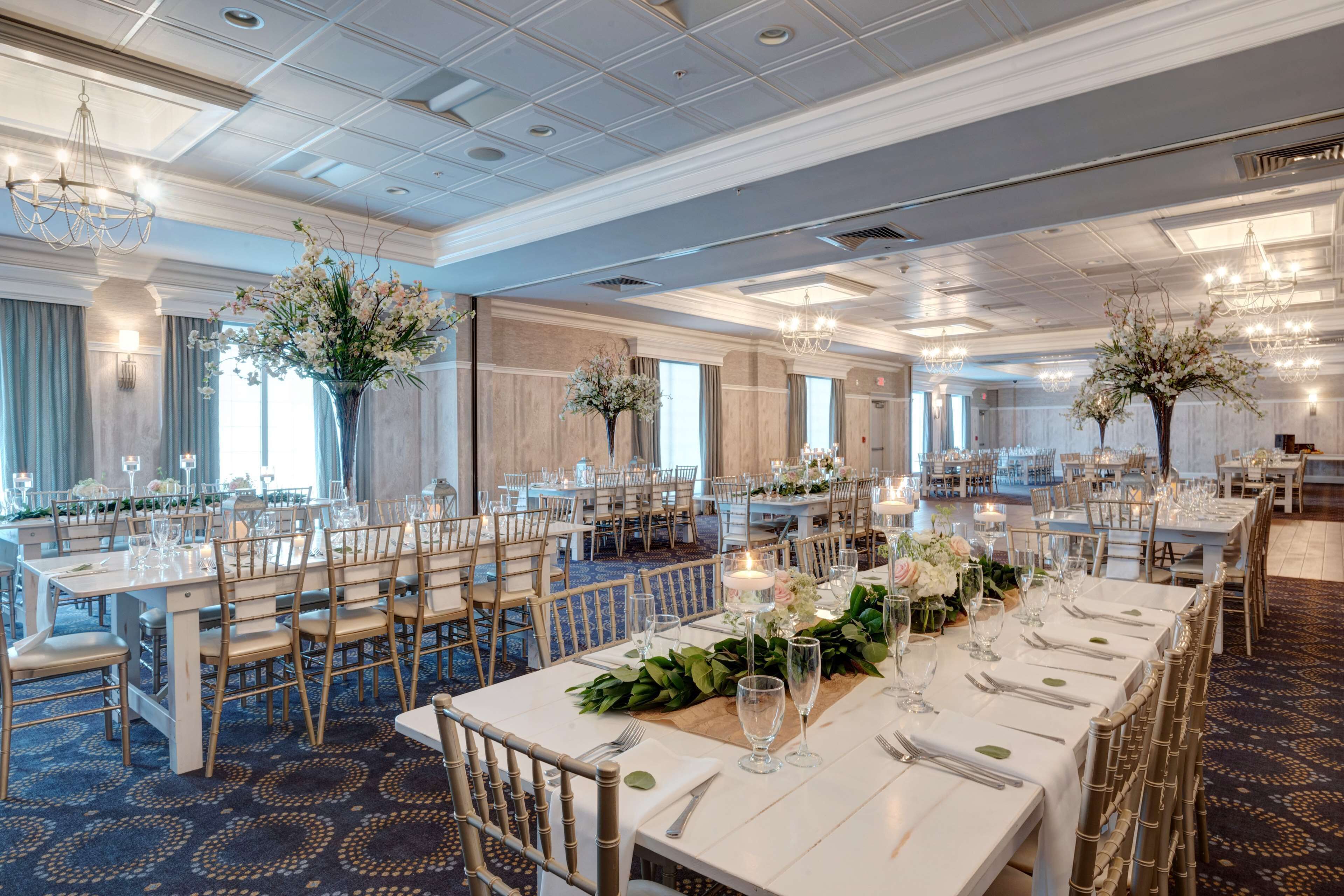 A spacious banquet hall with long tables set for dining, elegant chandeliers, and floral centerpieces.
