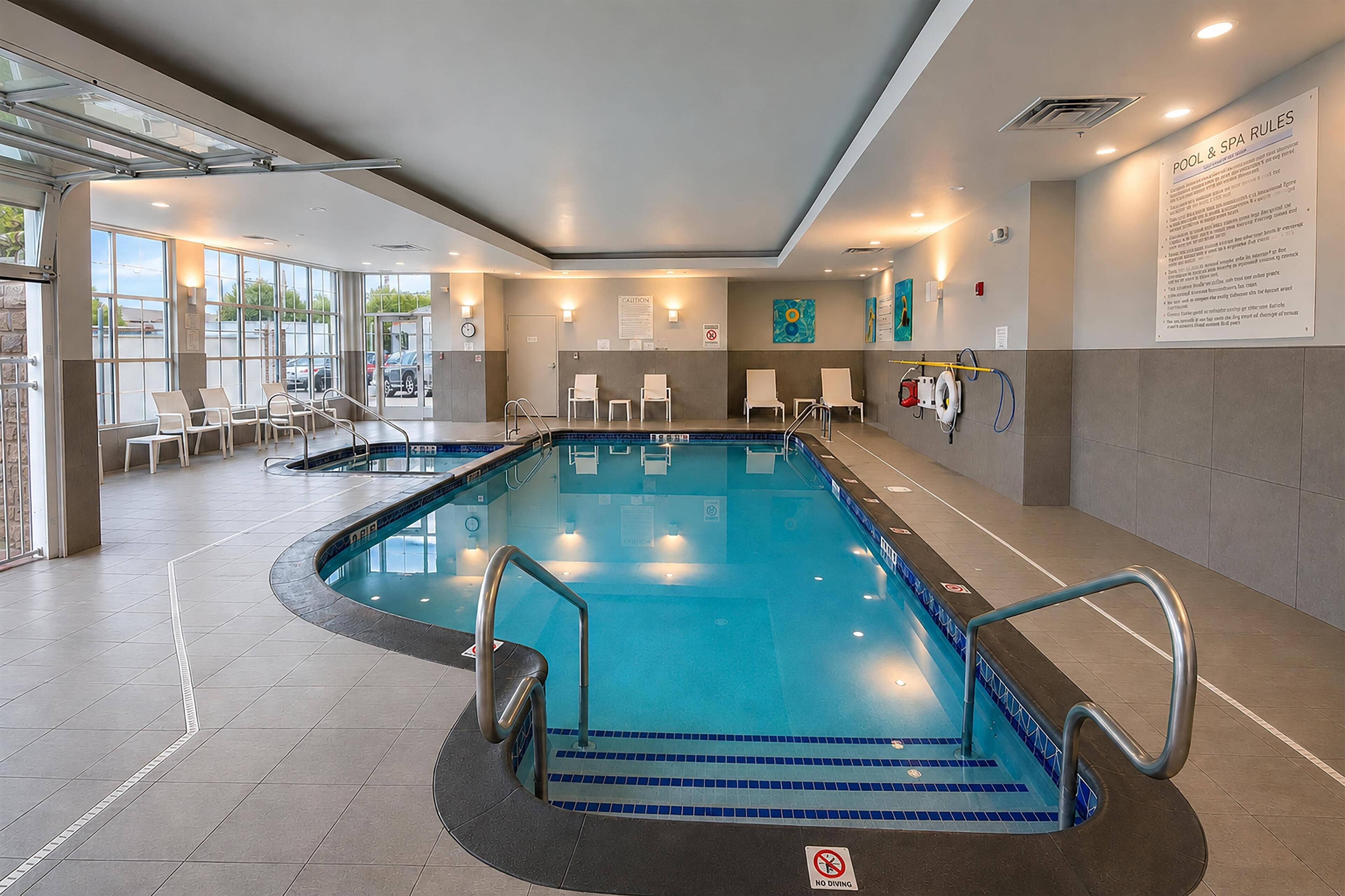 Una piscina interior con agua cristalina, un cartel que indica 'no buceo' y un cartel con las normas de la piscina en la pared.