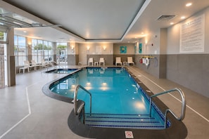 Una piscina interior con agua cristalina, un cartel que indica 'no buceo' y un cartel con las normas de la piscina en la pared.