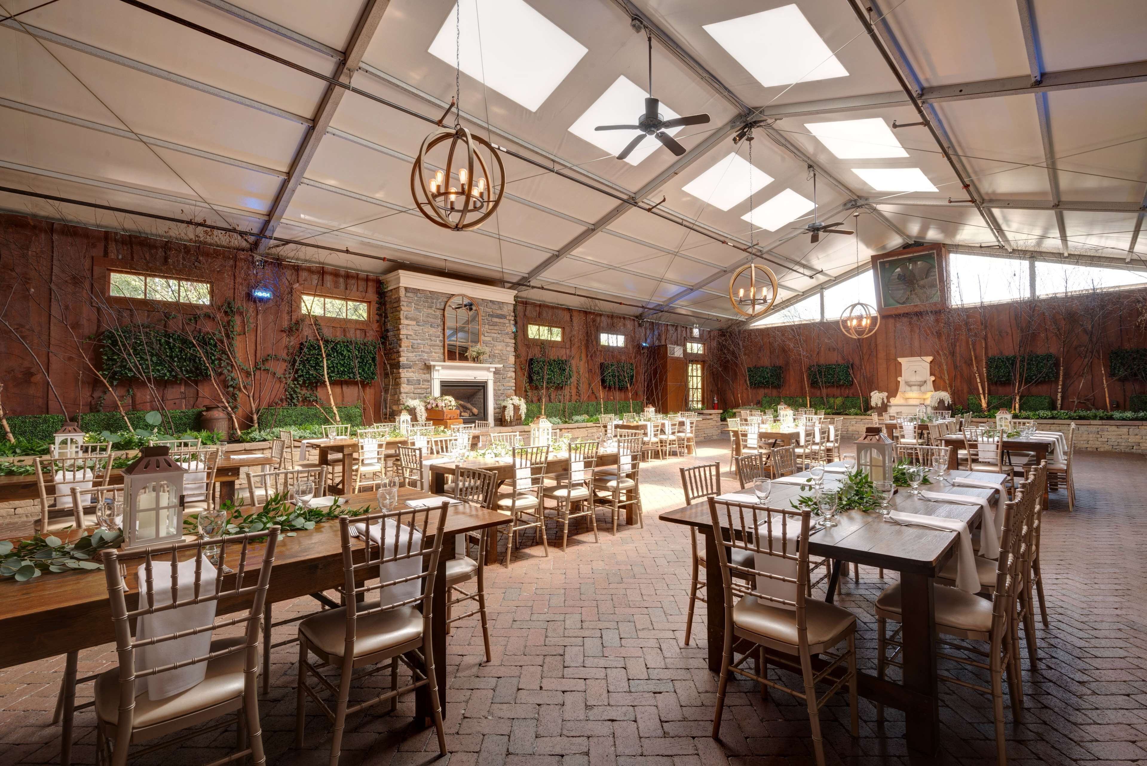 A spacious indoor dining area with multiple tables and chairs, a high ceiling with skylights, and a rustic wooden wall.