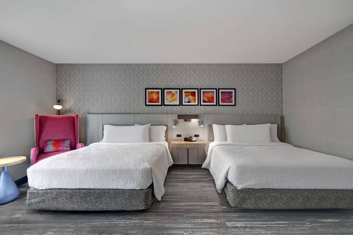 A hotel room with two beds, a desk, a chair, and a small table.