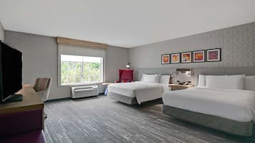 A hotel room with two beds, a desk with a TV, a window with a view, and a wall with framed pictures.