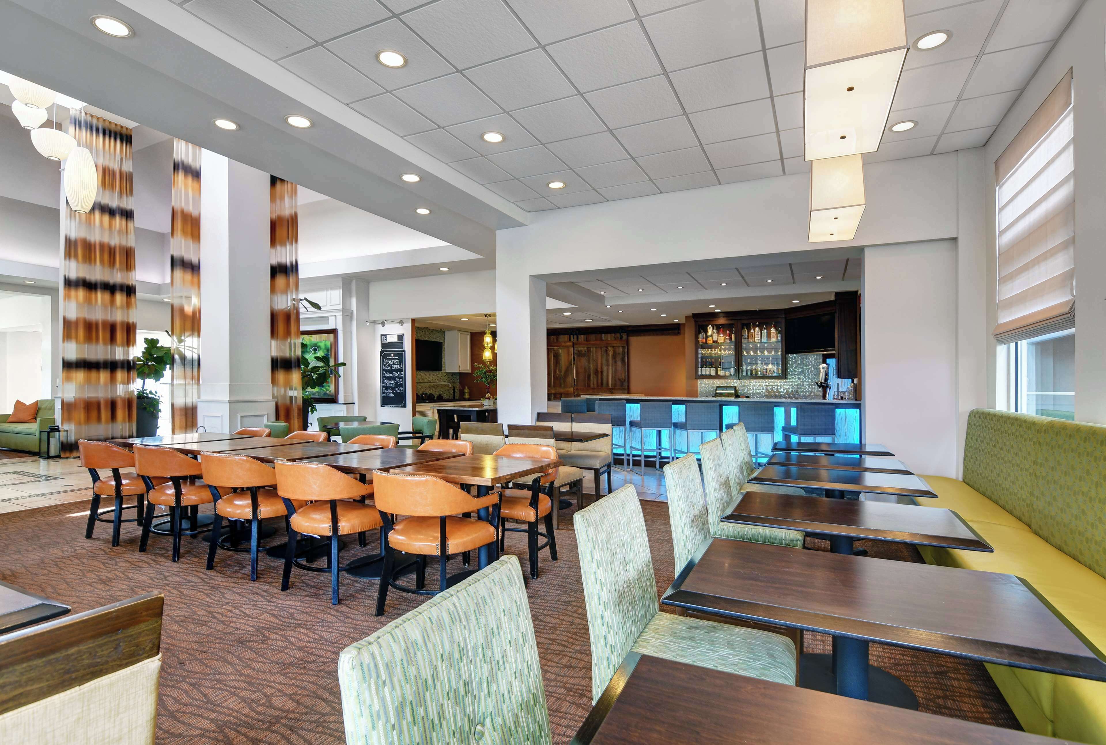 A spacious dining area with multiple tables and chairs, a bar area in the background, and a seating area with a green couch.