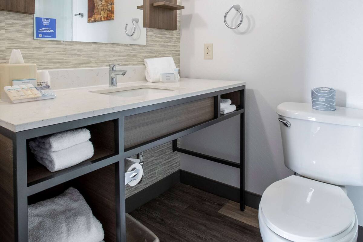 Un baño moderno con un espejo grande, un lavamanos, un inodoro y un perchero para toallas.