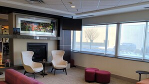 A modern lounge area with a fireplace, comfortable seating, and large windows offering a view of the outside. - Hilton Garden Inn Mankato Downtown (Mankato)