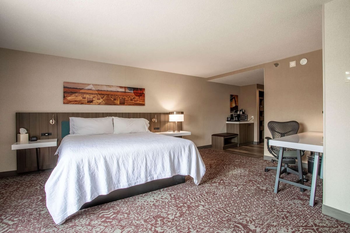 Una habitación de hotel con cama, mesita de noche, lámpara, escritorio, silla y un cuadro en la pared.