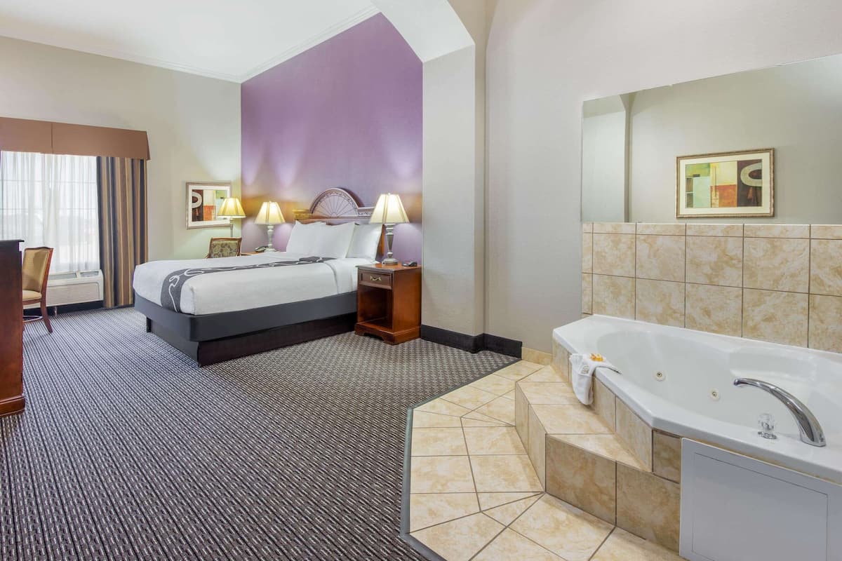 A hotel room with a large bed, two bedside lamps, a bathroom with a bathtub, and a large mirror.