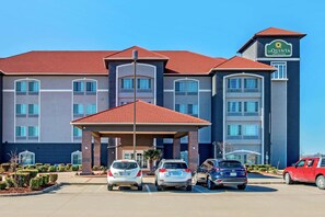 A hotel with a red-tiled roof, a covered entrance, and a parking lot with several cars.