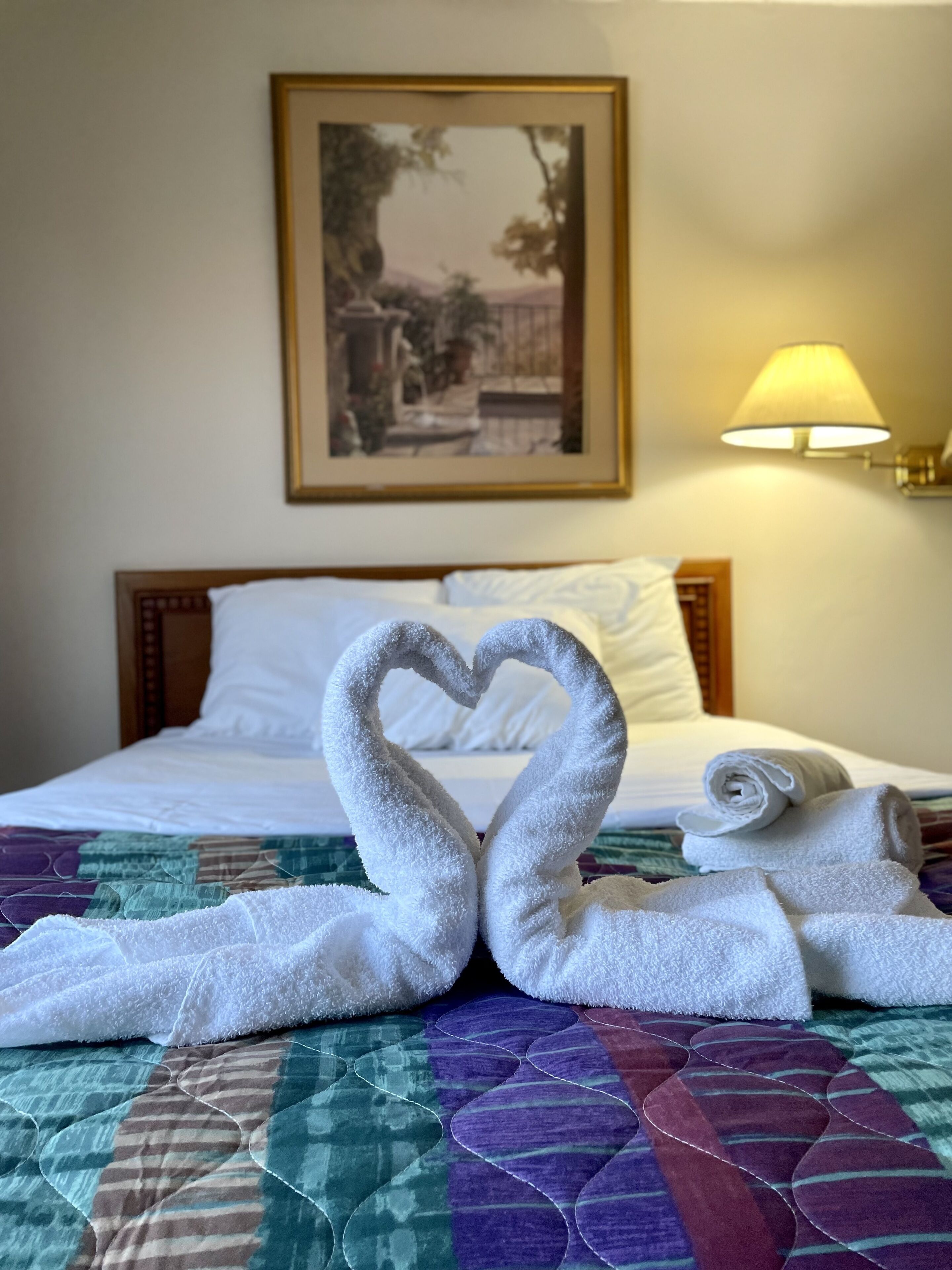 A hotel room with a bed, a painting on the wall, and a lamp.