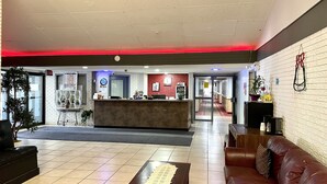 A hotel lobby with a reception desk, a red accent wall, a seating area with a brown leather sofa, and a tiled floor. - Lively Inn & Suites (Sudbury)