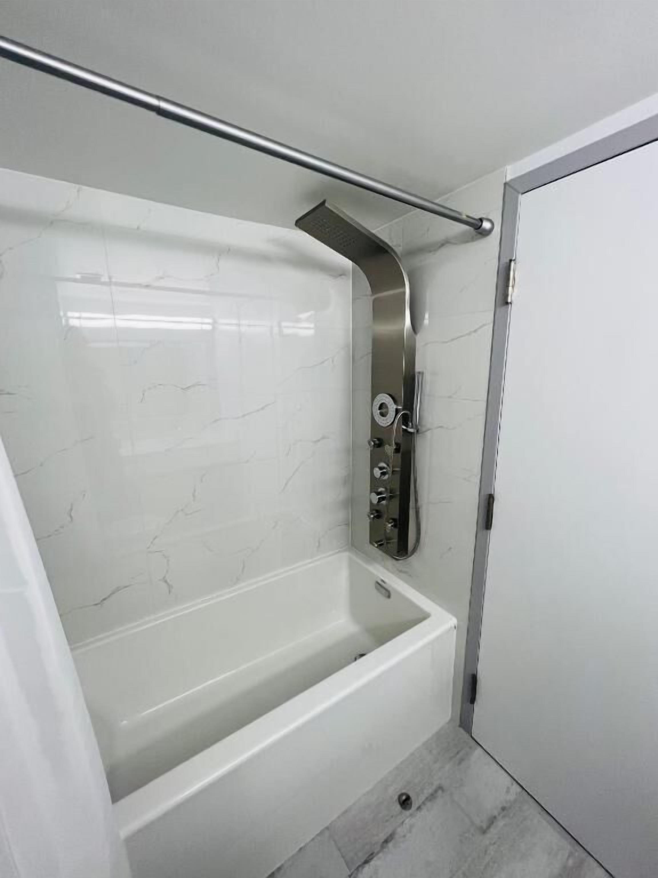 A bathroom with a white bathtub, a showerhead, and a door.