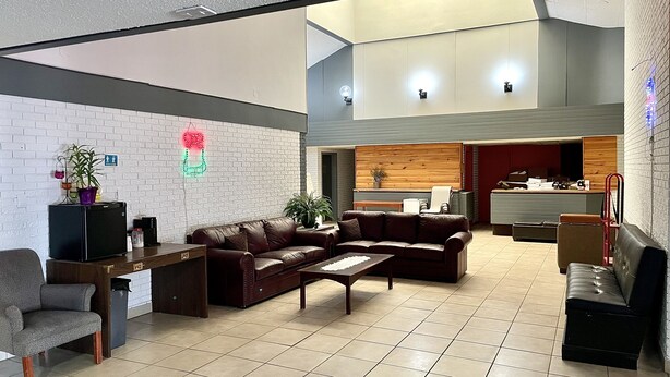 A modern lobby with a seating area, a reception desk, and a kitchen in the background. - Lively Inn & Suites (Sudbury)