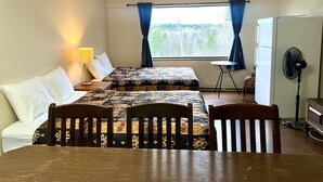 A room with two beds, a table, chairs, a lamp, a fan, and a window with curtains. - Lively Inn & Suites (Sudbury)