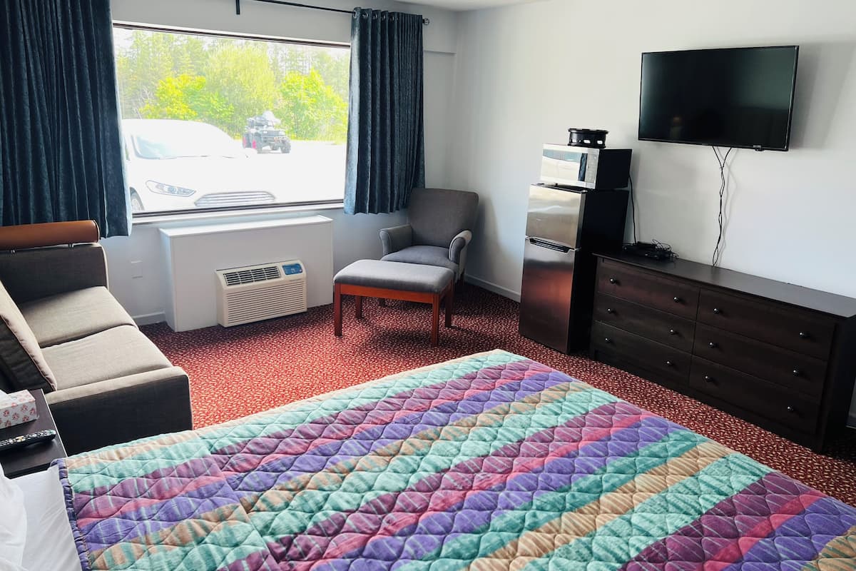 Habitación de hotel con cama, una silla, cómoda, televisor y ventana con cortinas.