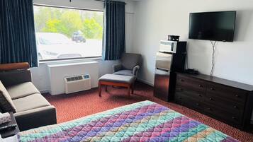Habitación de hotel con cama, una silla, cómoda, televisor y ventana con cortinas.